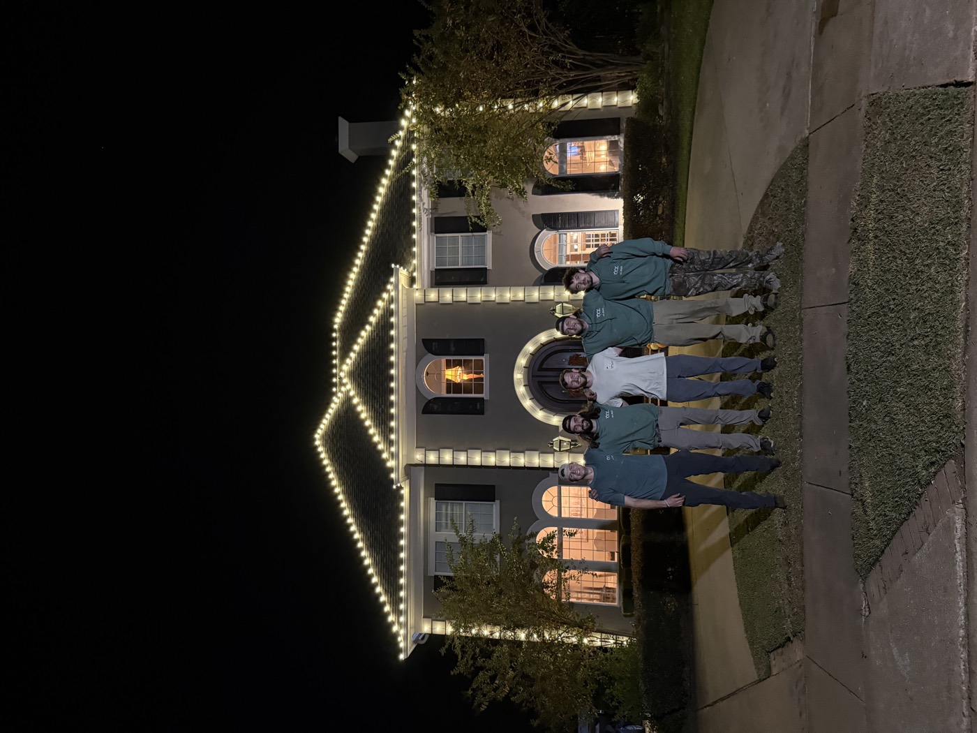 The Cajun Christmas Lights crew standing in front of a two-story home outlined in warm white lights