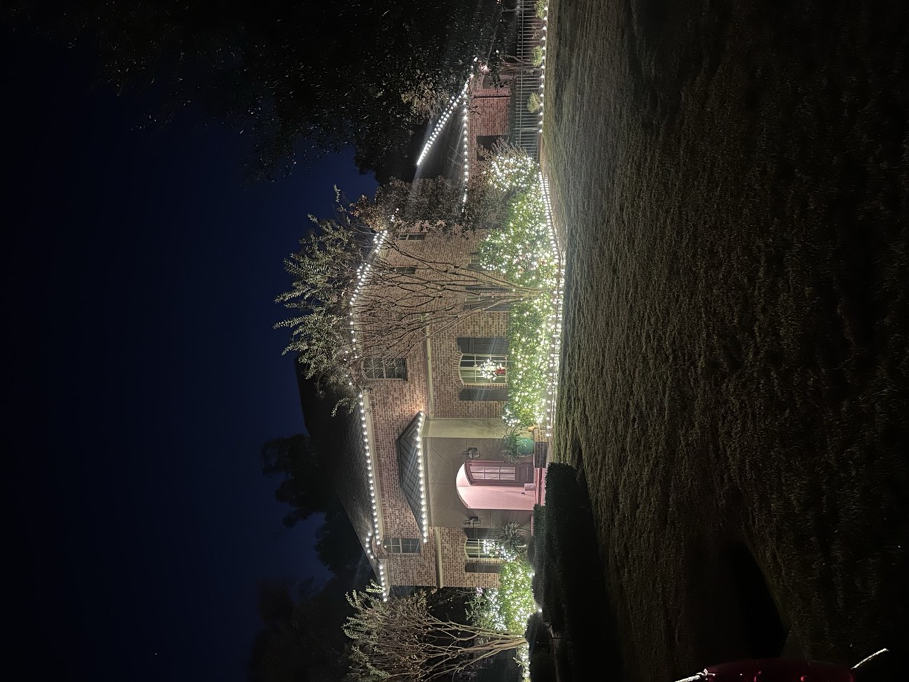 Front landscaping beds glowing with white net lights below a lit roofline