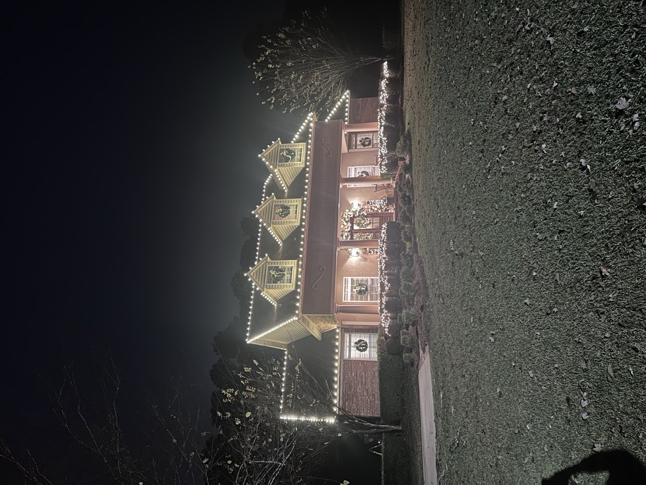 Two-story home with lit wreaths on the dormers and a decorated entry