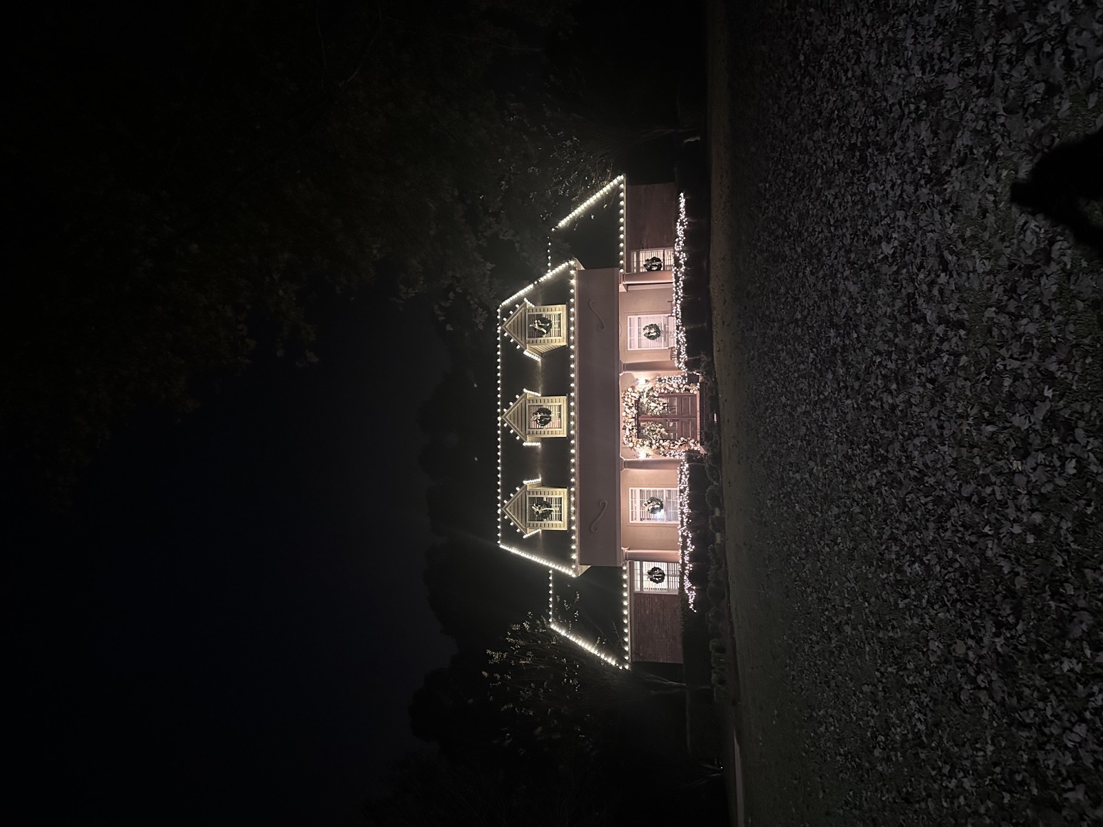 Home with lit dormer wreaths and a garland-framed entry