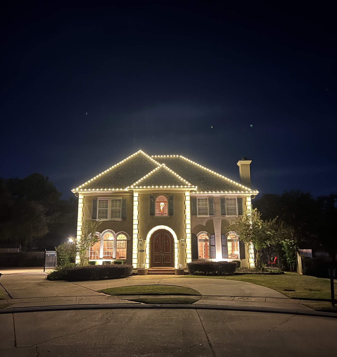 Stately two-story home with columns outlined in warm white lights